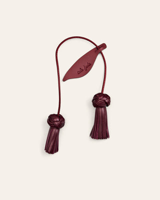 Cala Jade leather bag charm in burgundy red shaped as a flower on a beige background