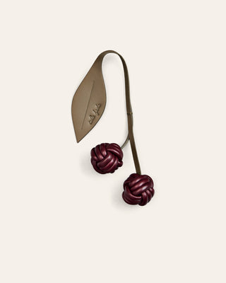 Cala Jade cherry bag charm on burgundy and green on a beige background