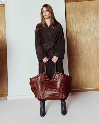 Woman holding a large brown textured bag indoors with wooden paneling.