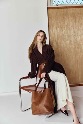 Woman holding a brown leather bag in a minimalistic setting