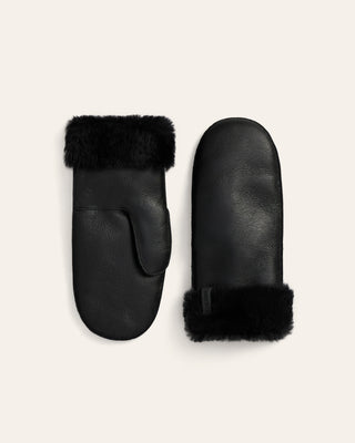 Pair of black leather mittens with fur trim on a beige background