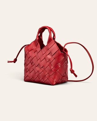 A red woven leather handbag with top handles and a shoulder strap, photographed on a clean off-white background.