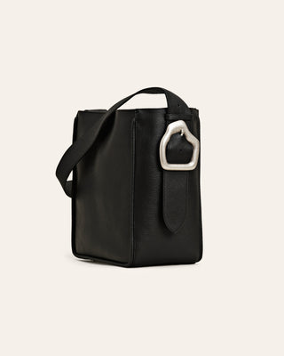 Cala Jade Masago black leather tote bag with a custommade silver buckle on a beige background