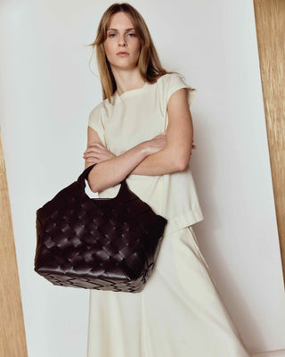 Woman holding a dark quilted handbag against a plain background