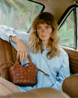 Woman sitting in a car holding a brown woven handbag