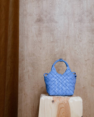 A blue woven leather bag on a wooden pidestal
