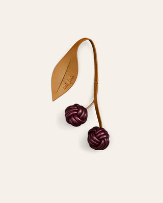 Cala Jade cherry leather bag charm in yellow and burgundy on a beige background