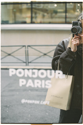 Person holding a camera with a 'Bonjour Paris' sign in the background