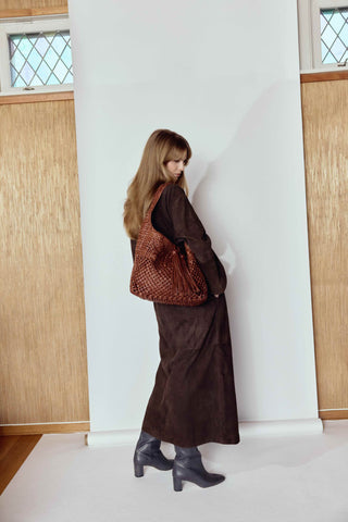 Woman in a brown dress holding a textured bag against a white wall with wooden panels.