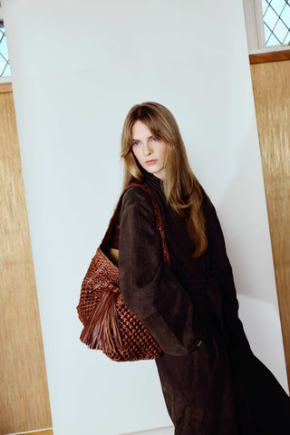 Woman holding a textured brown handbag against a white wall.