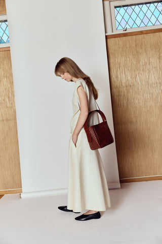 Woman in a long white dress holding a brown handbag in a room with a white photo paper background