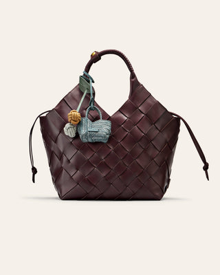 A burgundy woven leahter bag with bag charms attached on a beige background
