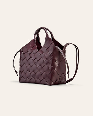 A woven butgundy leather bag on a beige background