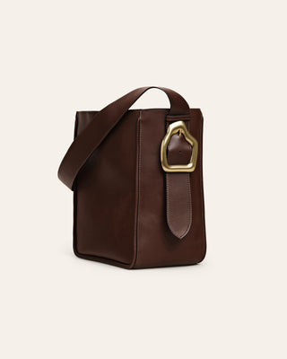 Brown leahter shoulder bag with a custommade gold buckle on beige background