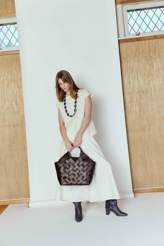 Woman in a white dress holding a black handbag in a minimalistic setting