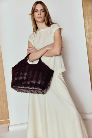 Woman holding a dark quilted handbag against a plain background