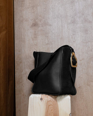 A black leather tote bag on a wooden pidestal