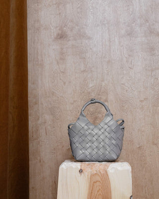 a grey leather bag on a wooden pidestal