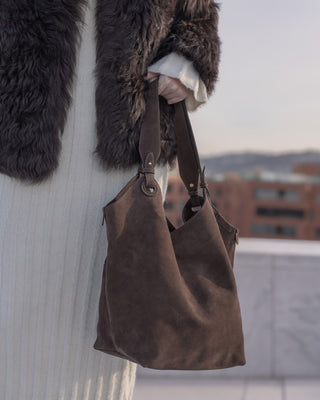 Brown leather handbag held by a person wearing a fur coat against a blurred urban background.