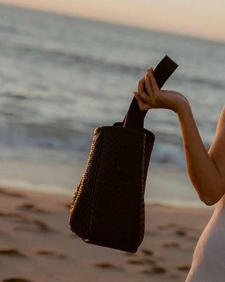 A woman holding a brown handbag in one hand on the beach